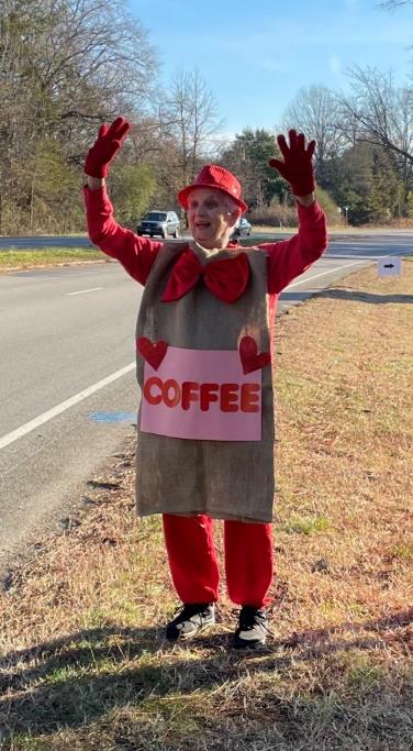 Susan Coleman stands by Huguenot Road Baptist church wearing a sign that says "coffee" with hearts on it.