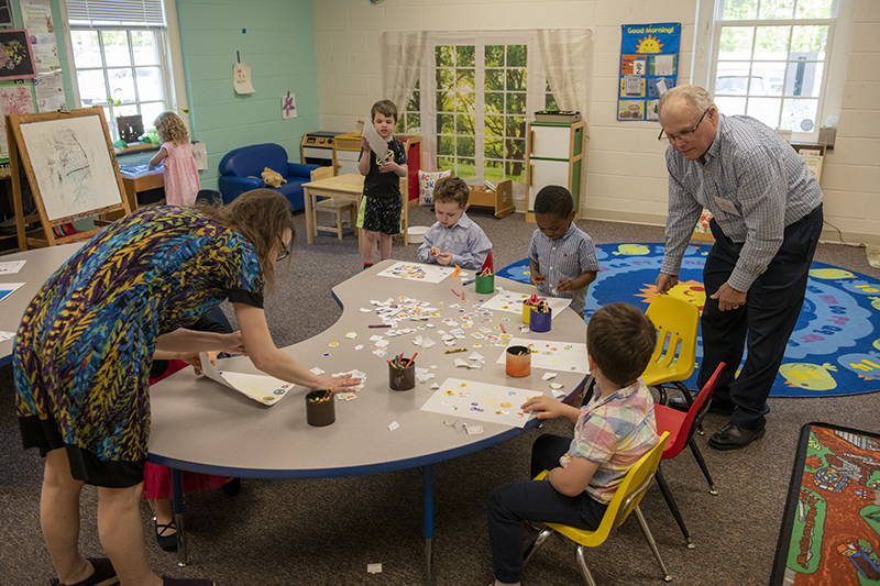 2 adults help children who are working at a table in a classroom at HRBC.