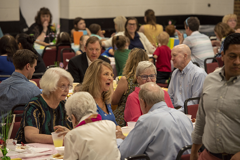 People eat and talk around large tables during a lunch at Huguenot Road Baptist Church